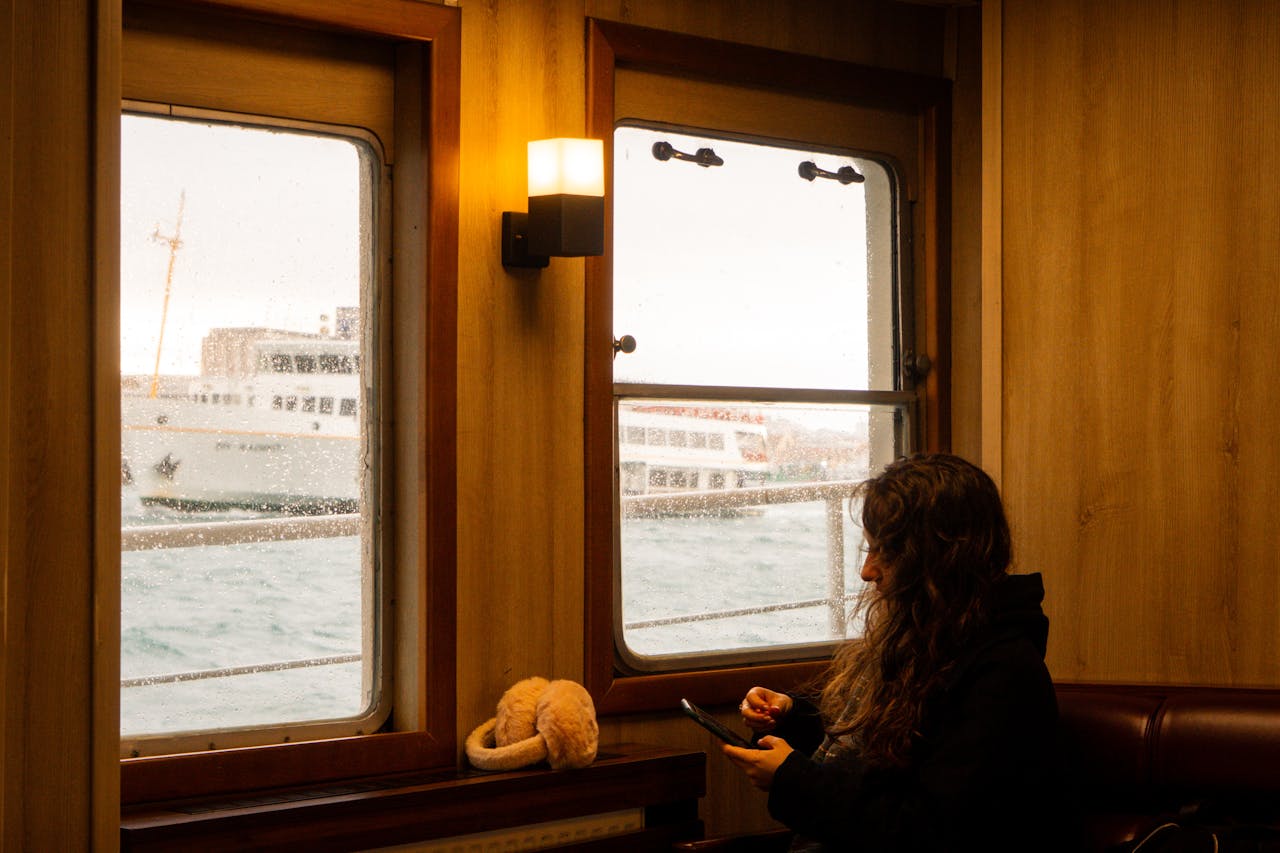 The Art of Drawing Readers In: Your attractive post title goes here Woman sitting inside a ferry with ocean view and boats visible through window.