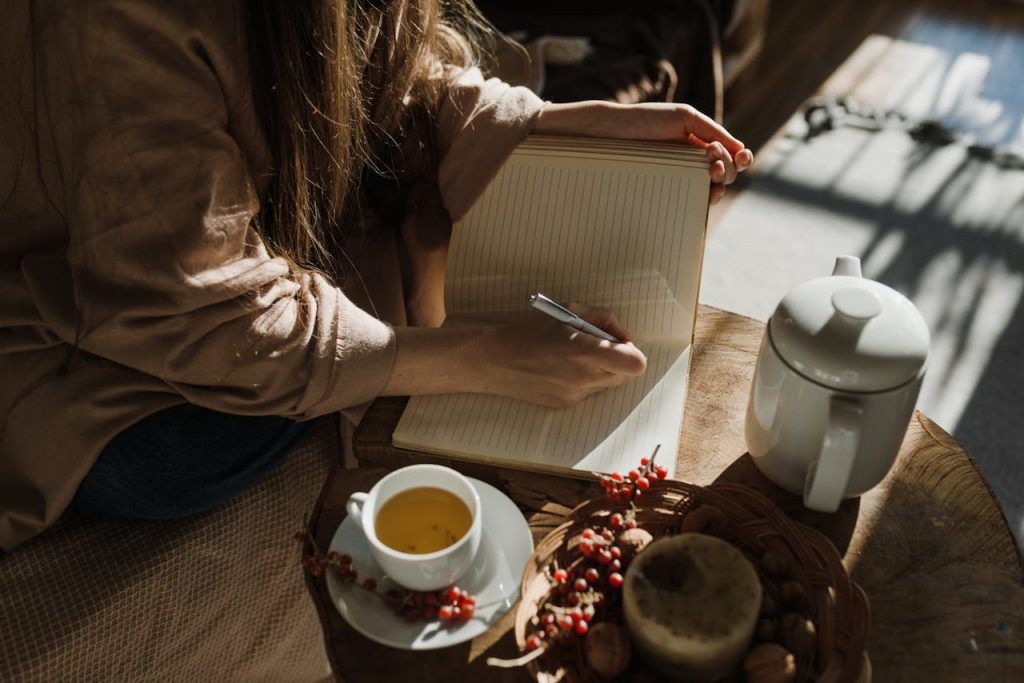 A person writes in a notebook while enjoying tea in natural light. Cozy and serene ambiance.